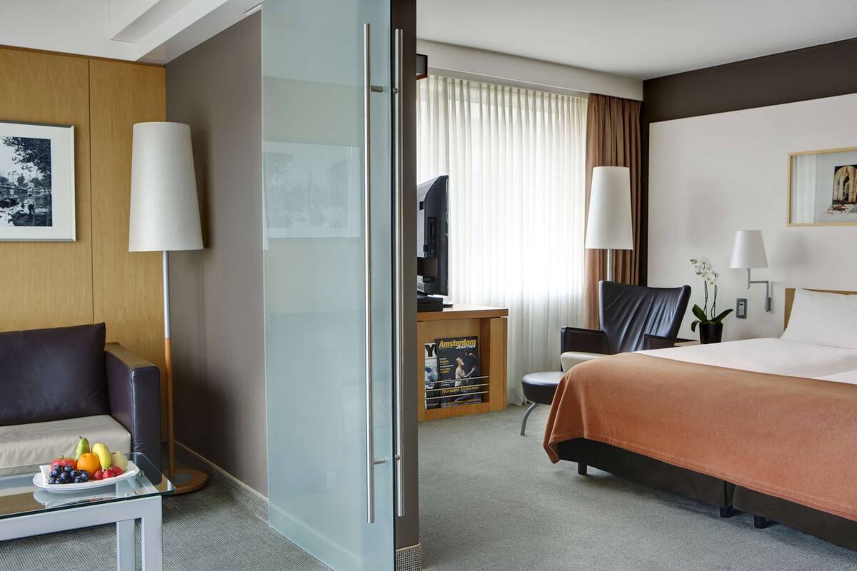Habitación de hotel con cama, escritorio con computadora, silla, sofá y un separador de vidrio.