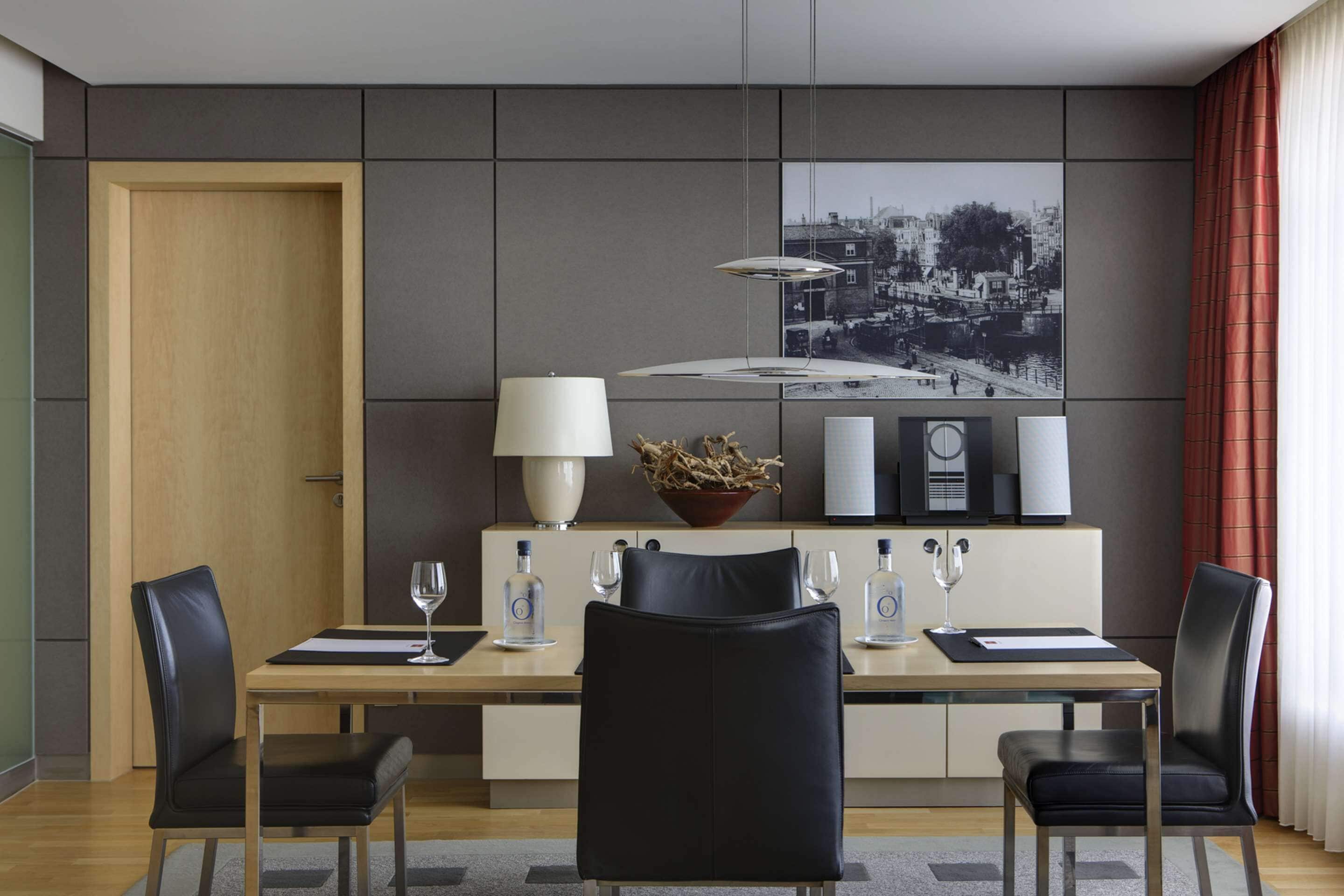 A modern dining area with a wooden table, black chairs, a white lamp, and a black and white cityscape artwork on the wall.