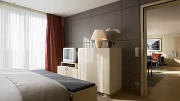 A hotel room with a bed, a desk, a television, a lamp, and a potted plant.