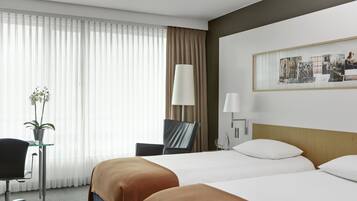 Habitación de hotel con dos camas, un escritorio, una silla, una lámpara y un cuadro en la pared.