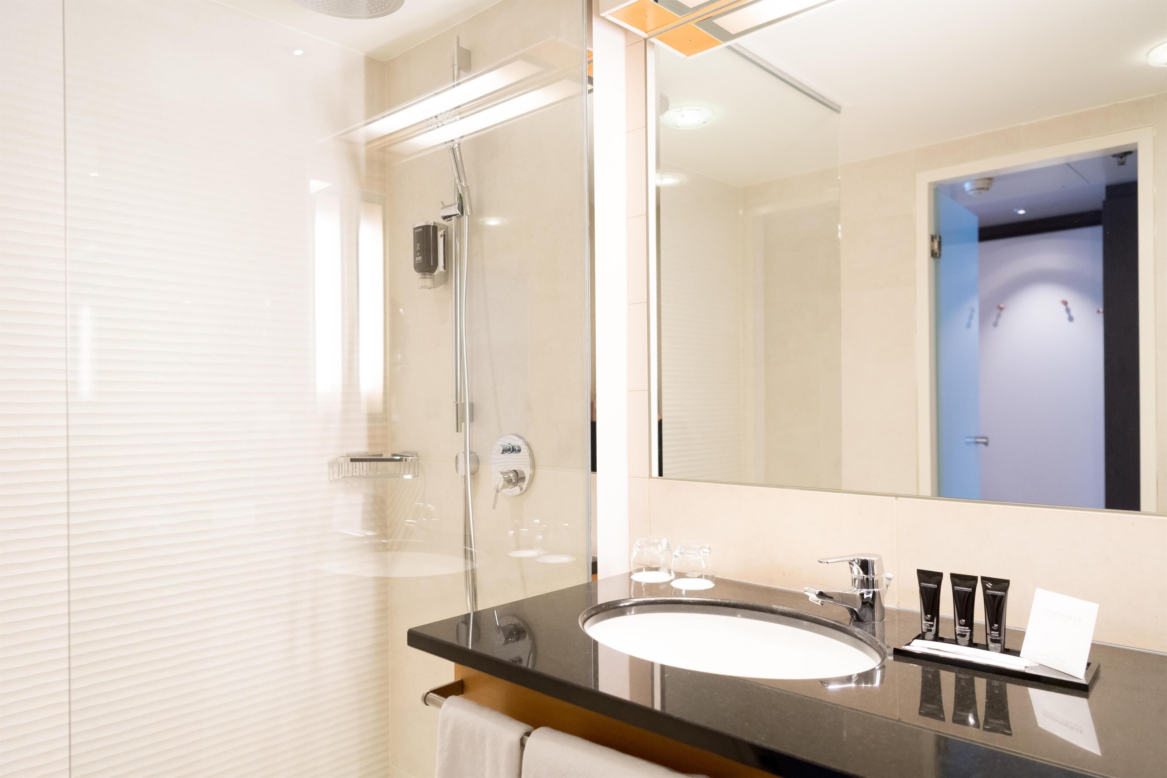 A modern bathroom with a glass shower enclosure, a large mirror, and a black countertop with a white sink.