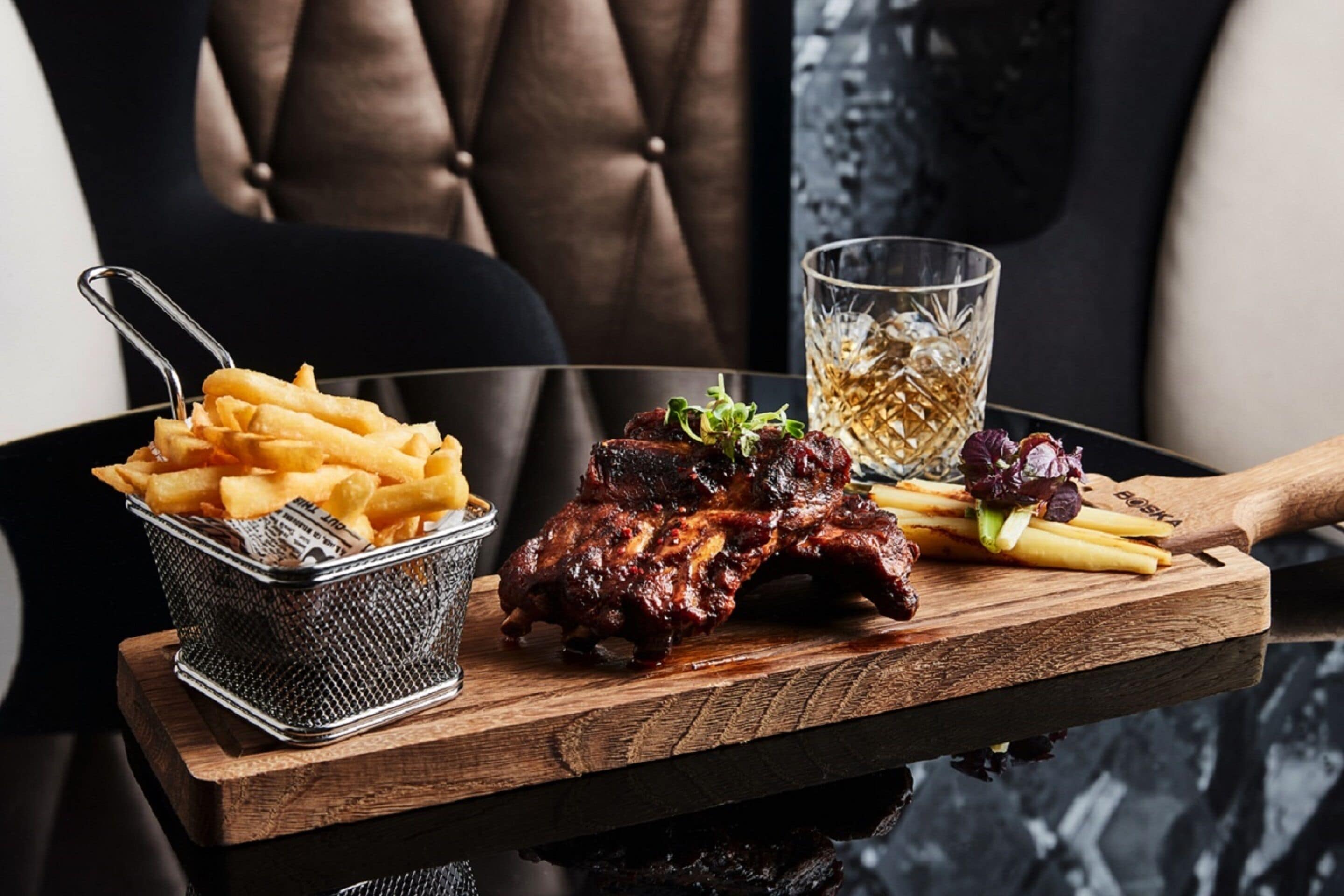 Een dienblad met ribben, friet en een drankje op een houten tafel.