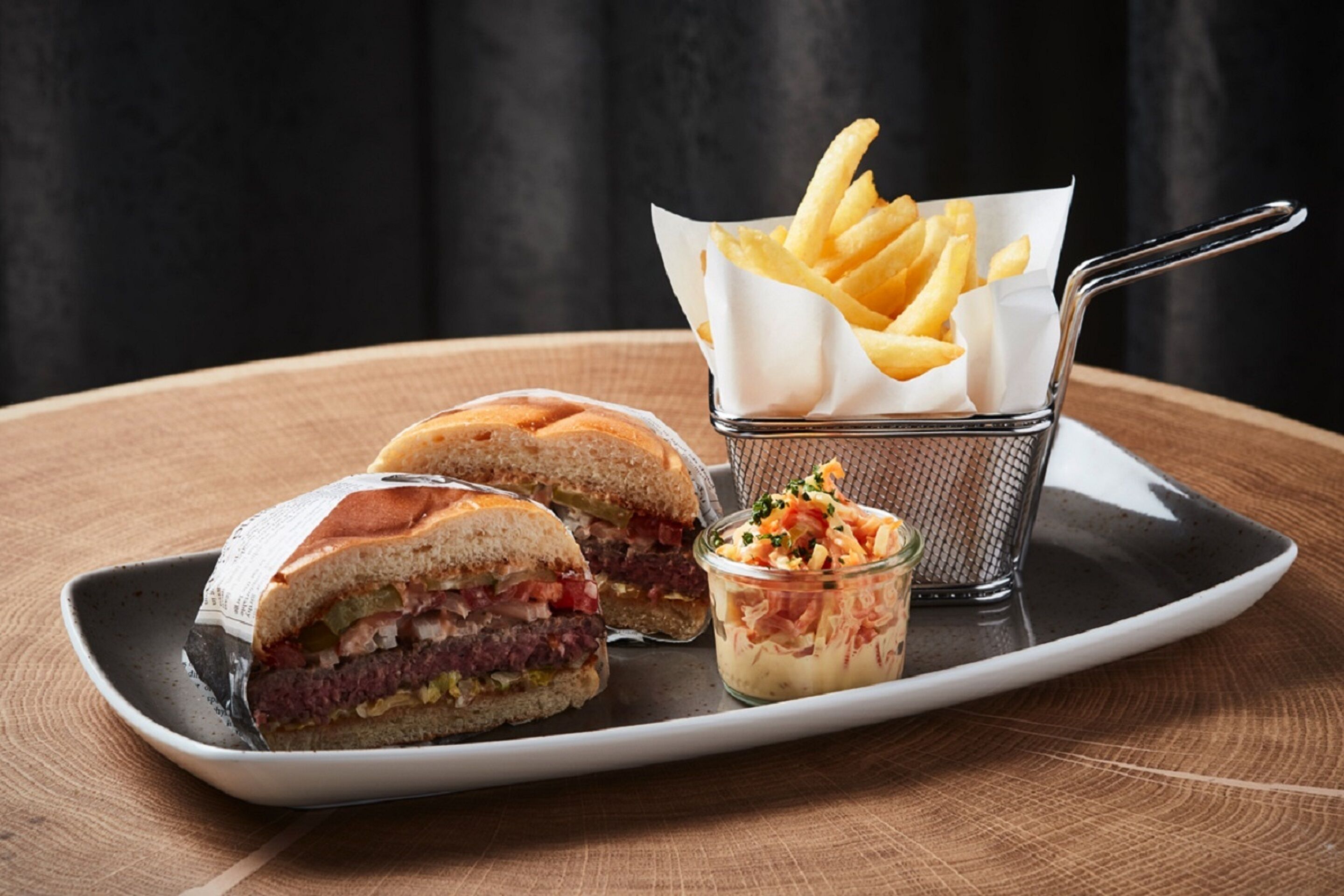 Ein halbiertes Sandwich, eine kleine Portion Pommes und eine kleine Salat-Schale auf einem Teller.