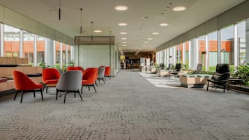 A spacious indoor area with seating arrangements, large windows, and a ceiling with recessed lighting.
