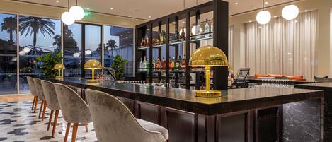 A bar area with a long counter, multiple bar stools, and a variety of bottles.