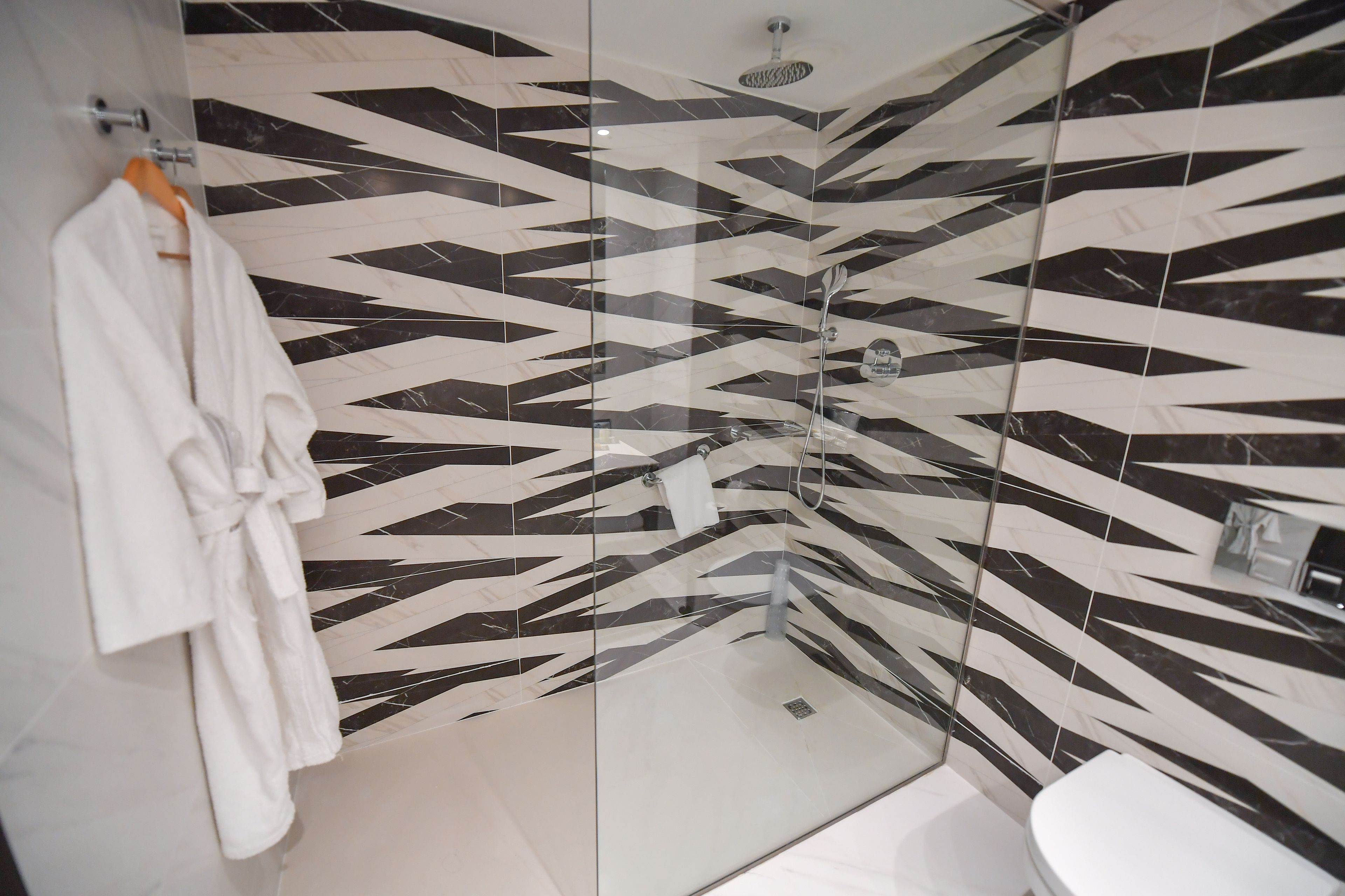 A modern bathroom with a geometric black and white tile design, a glass shower enclosure, and a white toilet.