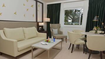 A hotel room with a beige sofa, a small round table with a vase of flowers, a chair, and a lamp.