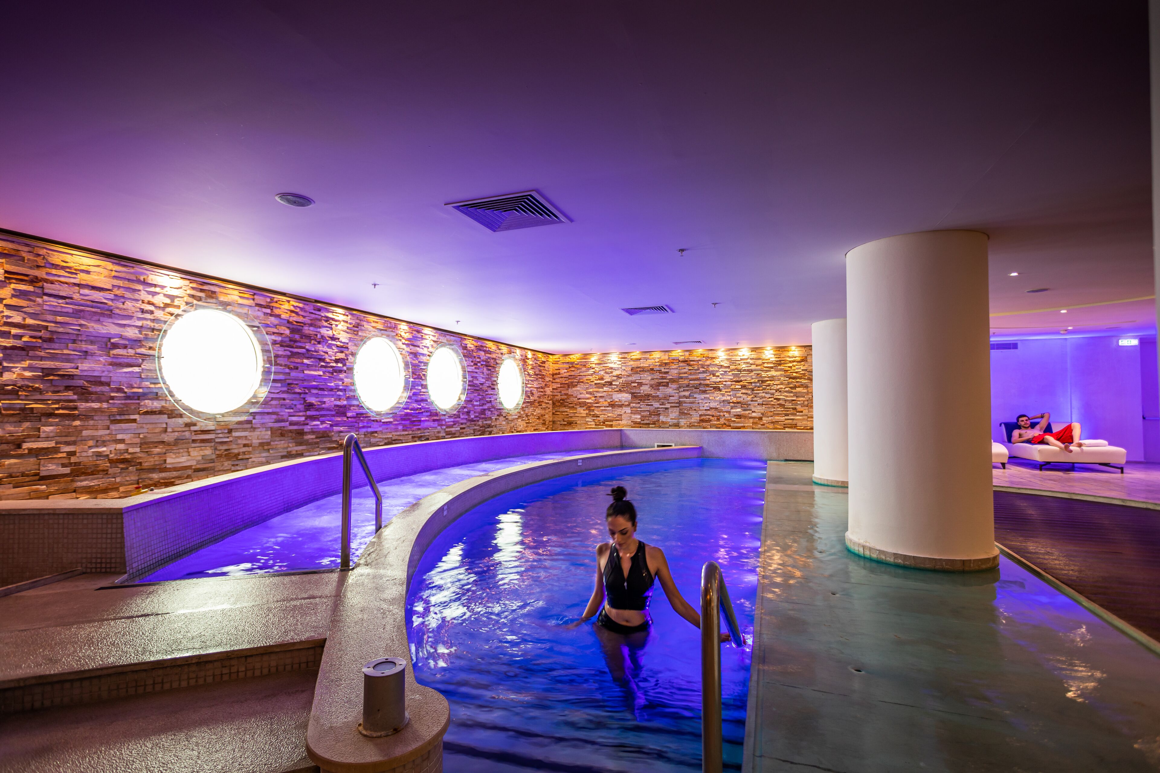 A swimming pool area with a stone wall and circular lights.