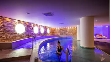 A swimming pool area with a stone wall and circular lights.
