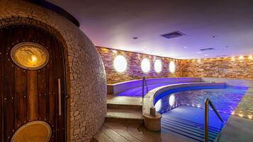 Un área de spa con pared de piedra, puerta de madera y piscina con escalones de acceso.