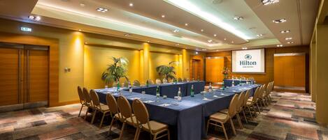 A conference room with a long table, chairs, and a projector screen displaying the Hilton logo.