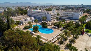 Un hotel con piscina central, varios pisos y un área ajardinada circundante con palmeras.