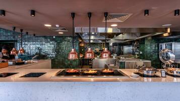 Una cocina moderna con lámparas colgantes de cobre, electrodomésticos de acero inoxidable y salpicadero con azulejos verdes.
