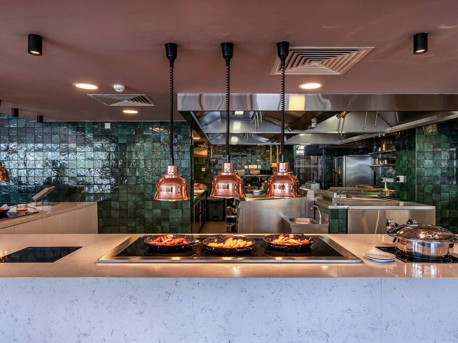 Una cocina moderna con lámparas colgantes de cobre, electrodomésticos de acero inoxidable y salpicadero con azulejos verdes.
