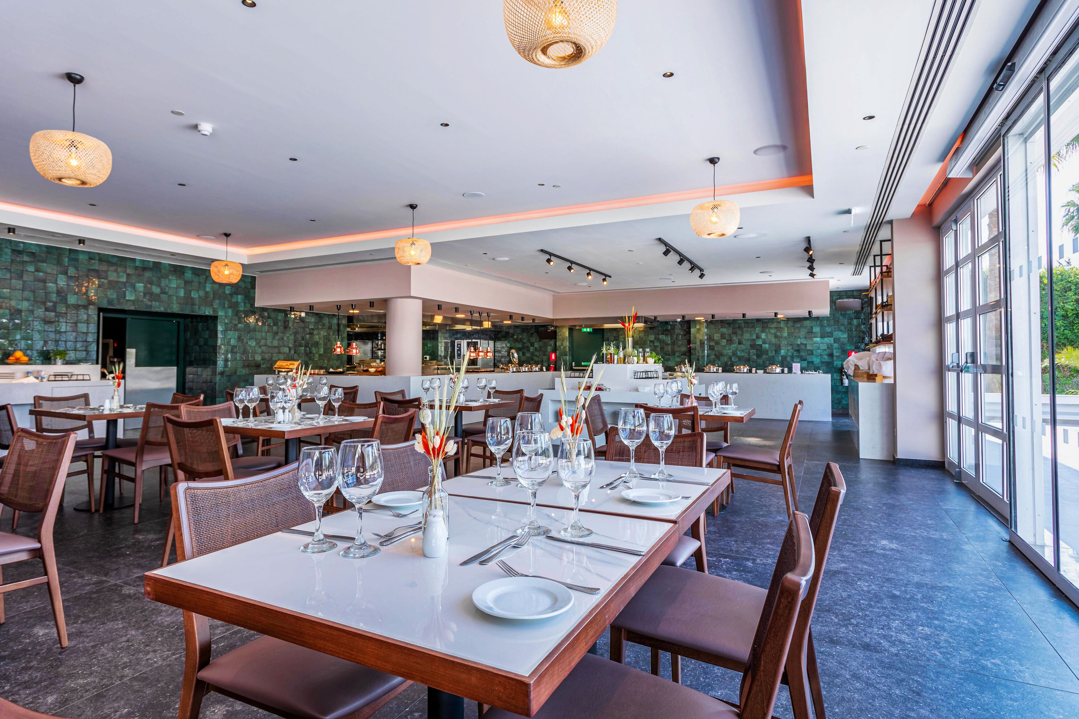 A restaurant with tables set for dining, a kitchen area, and large windows offering a view.