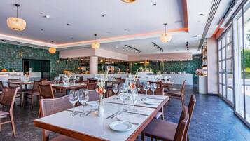 A restaurant with tables set for dining, a kitchen area, and large windows offering a view.