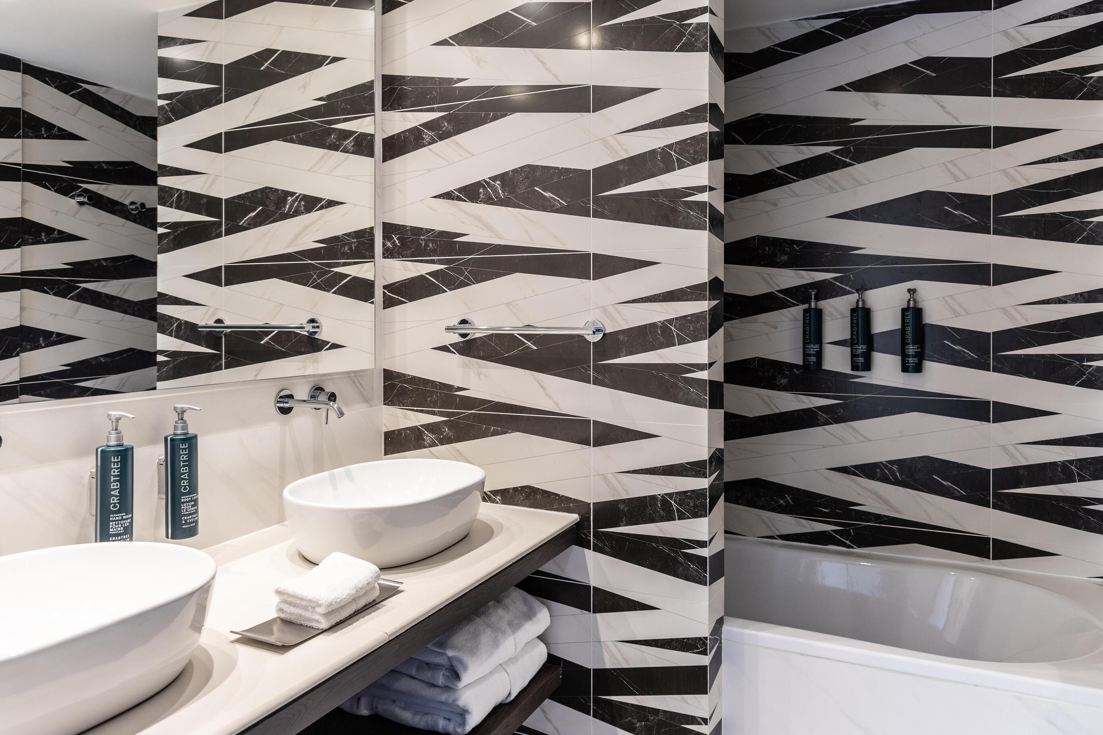A modern bathroom with black and white marble tiles, two sinks, a bathtub, and toiletries on the counter.