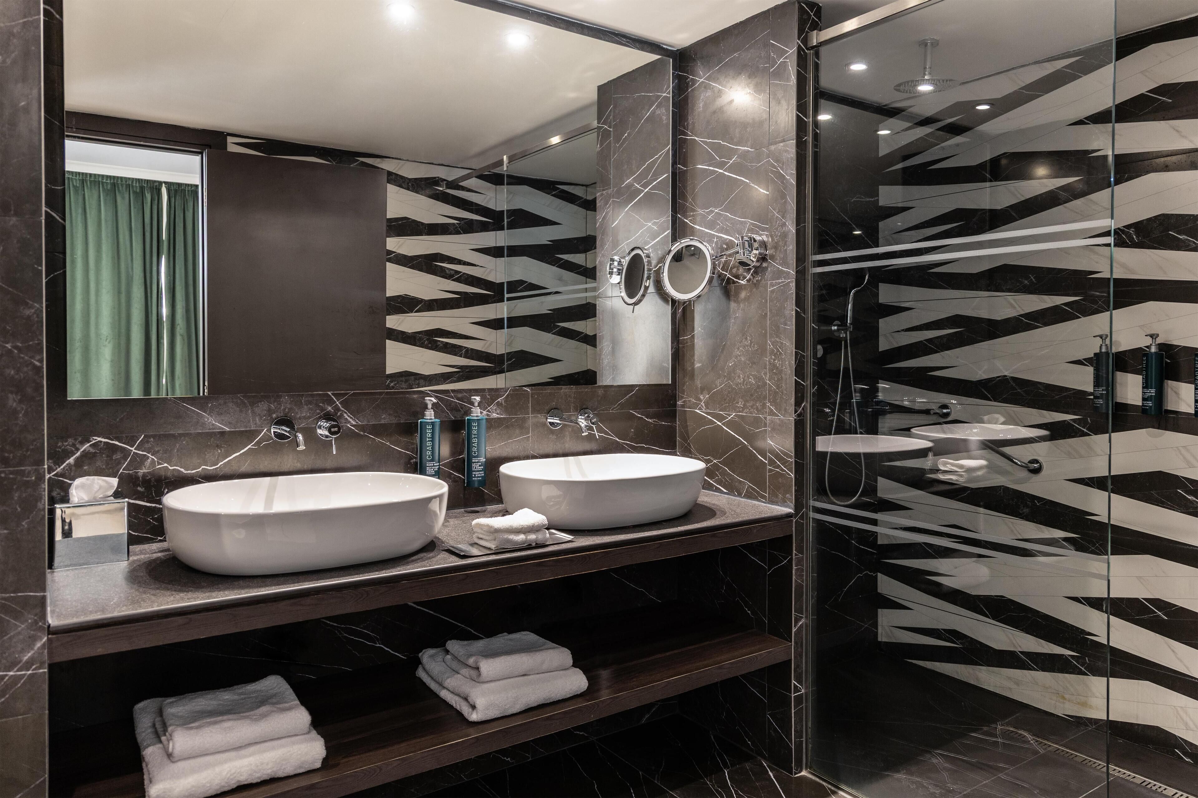 A modern bathroom with two large sinks, a glass shower enclosure, and a marble-patterned wall.