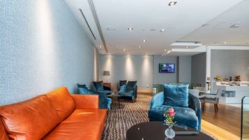 A modern hotel lobby with leather sofas, a round coffee table, and a TV mounted on the wall.