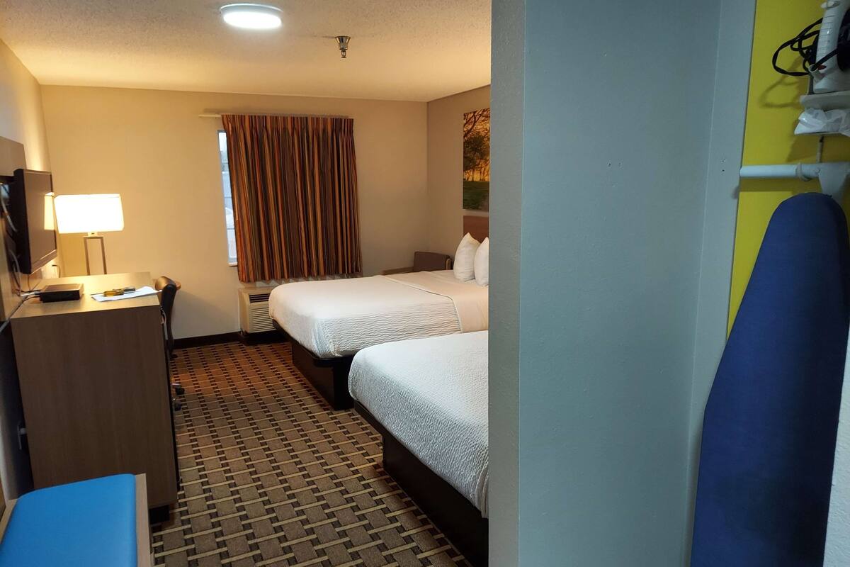 A hotel room with two beds, a desk with a lamp, a TV, and a window with curtains.