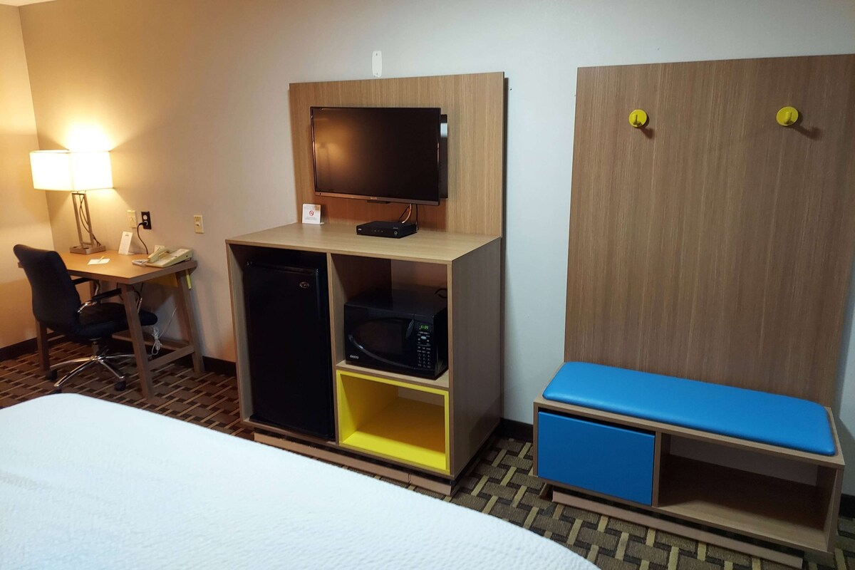 A hotel room with a bed, a desk with a computer, a television, a microwave, and a small seating area.