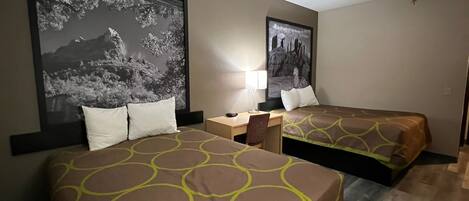 A hotel room with two beds, a desk, and a chair. There are two large framed pictures on the walls.