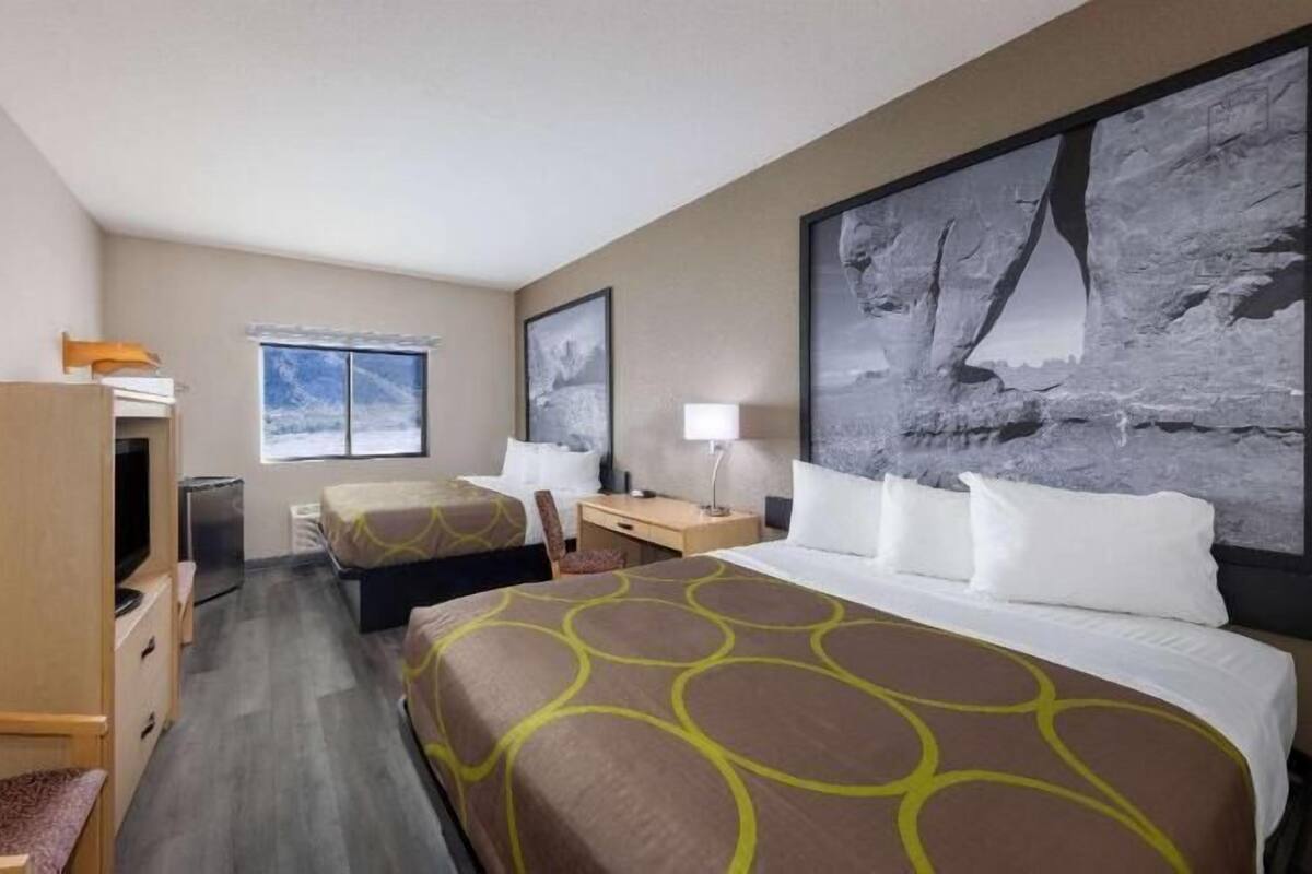 A hotel room with two beds, a desk, a chair, a TV, and large artwork on the walls.