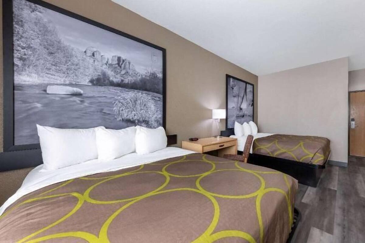 A hotel room with a large bed, a smaller bed, a desk, a chair, a TV, and artwork on the walls.