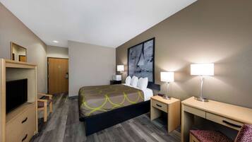 A hotel room with a bed, a desk, a chair, a TV, and a painting on the wall.