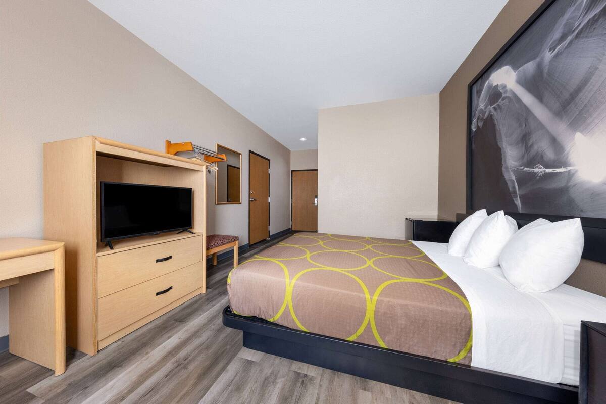 A hotel room with a bed, a desk, a television, and a door.