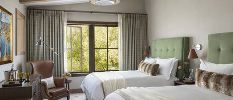 A hotel room with two beds, a desk, a chair, a lamp, and a window with curtains.