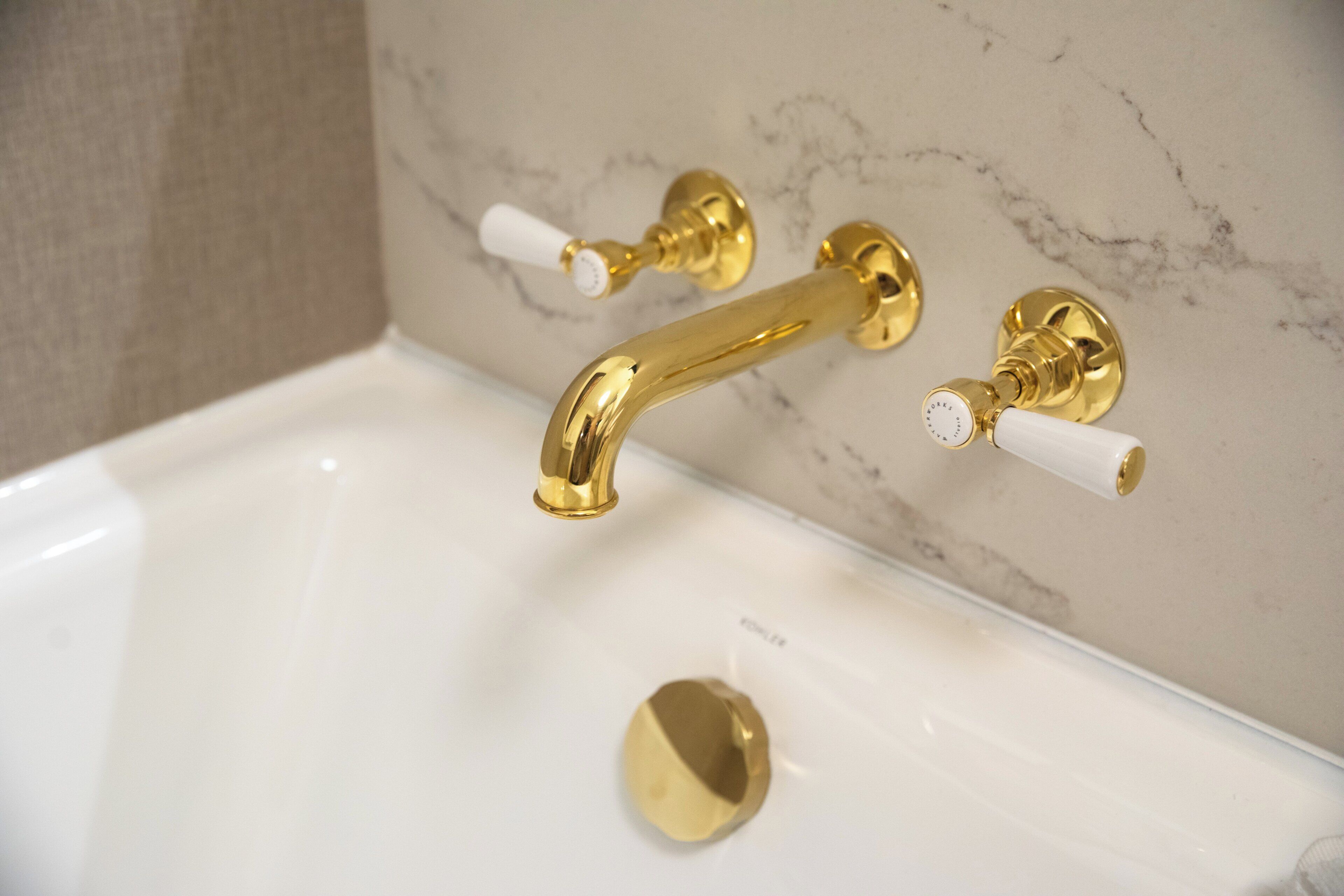 A bathtub with gold fixtures and white handles.