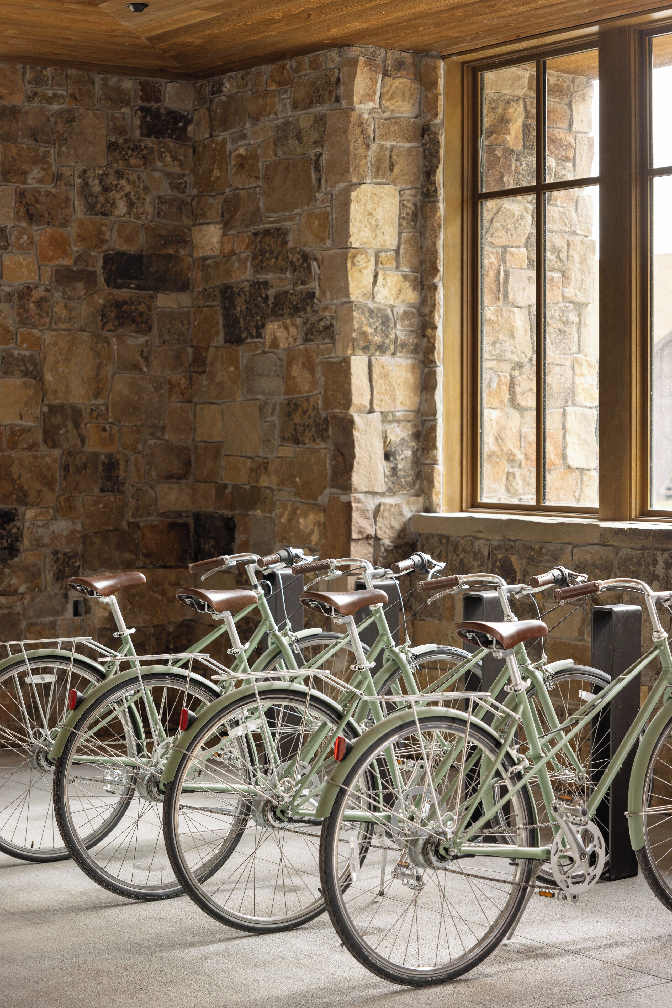Une rangée de vélos anciens est garée contre un mur de pierre dans une pièce dotée d’une grande fenêtre.