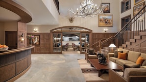 A spacious lobby with a curved reception desk, a chandelier, a staircase, and a dining area with tables and chairs. - The Rusty Parrot Lodge and Spa (Jackson)