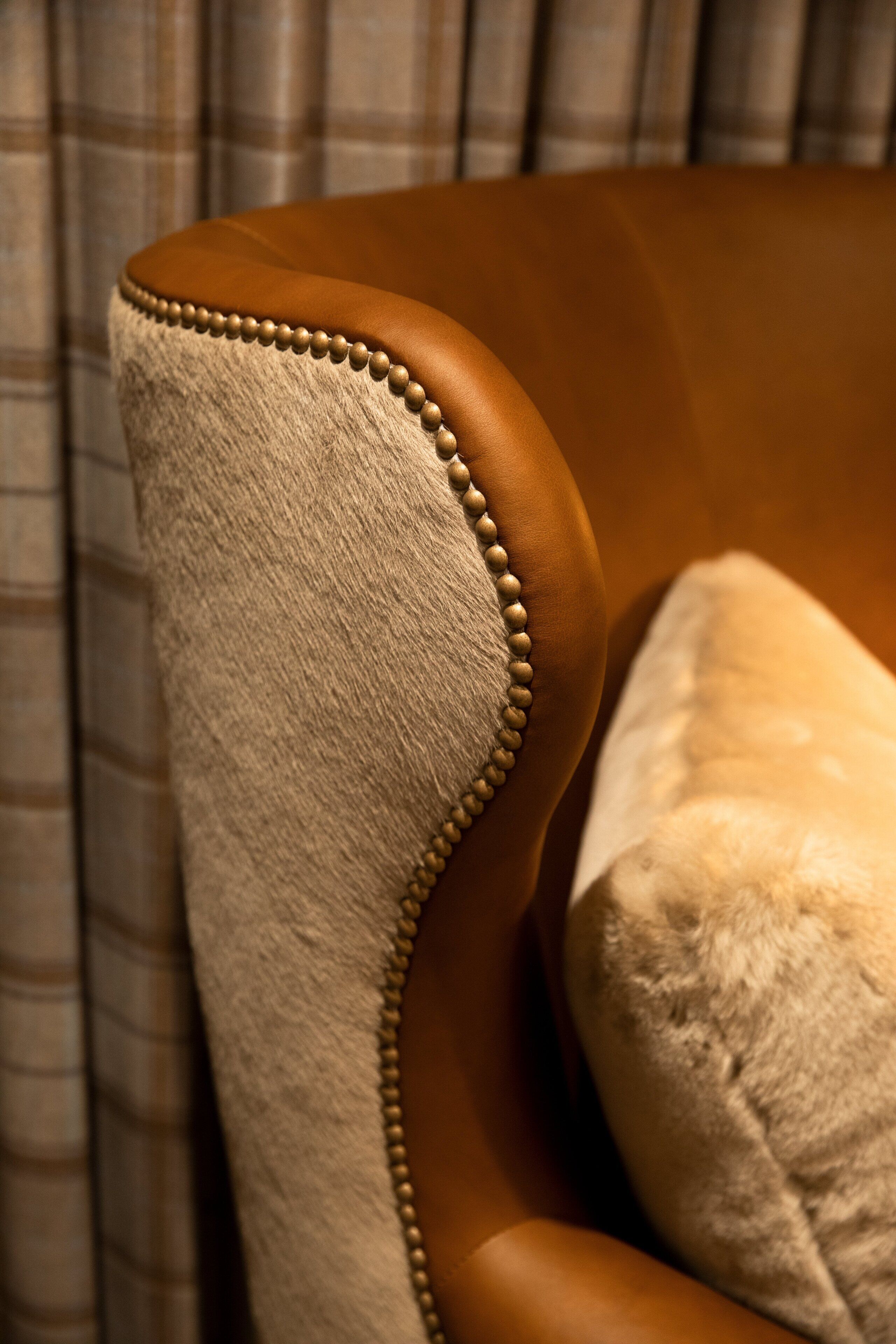 Gros plan d’une chaise avec un dossier en cuir marron et un accoudoir recouvert d’un tissu beige, agrémenté d’une bordure ornée de perles.