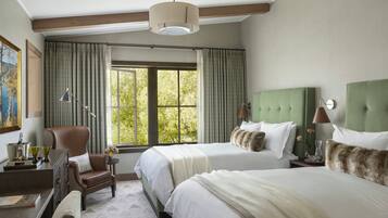 A hotel room with two beds, a desk, a chair, a lamp, and a window with curtains.