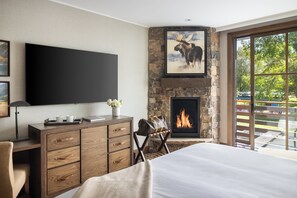 A bedroom with a large bed, a TV mounted on the wall, a fireplace, and a view of the outdoors. - The Rusty Parrot Lodge and Spa (Jackson)