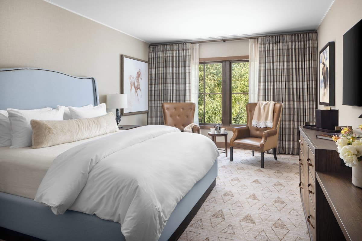 A hotel room with a large bed, a desk, a chair, and a window with curtains.