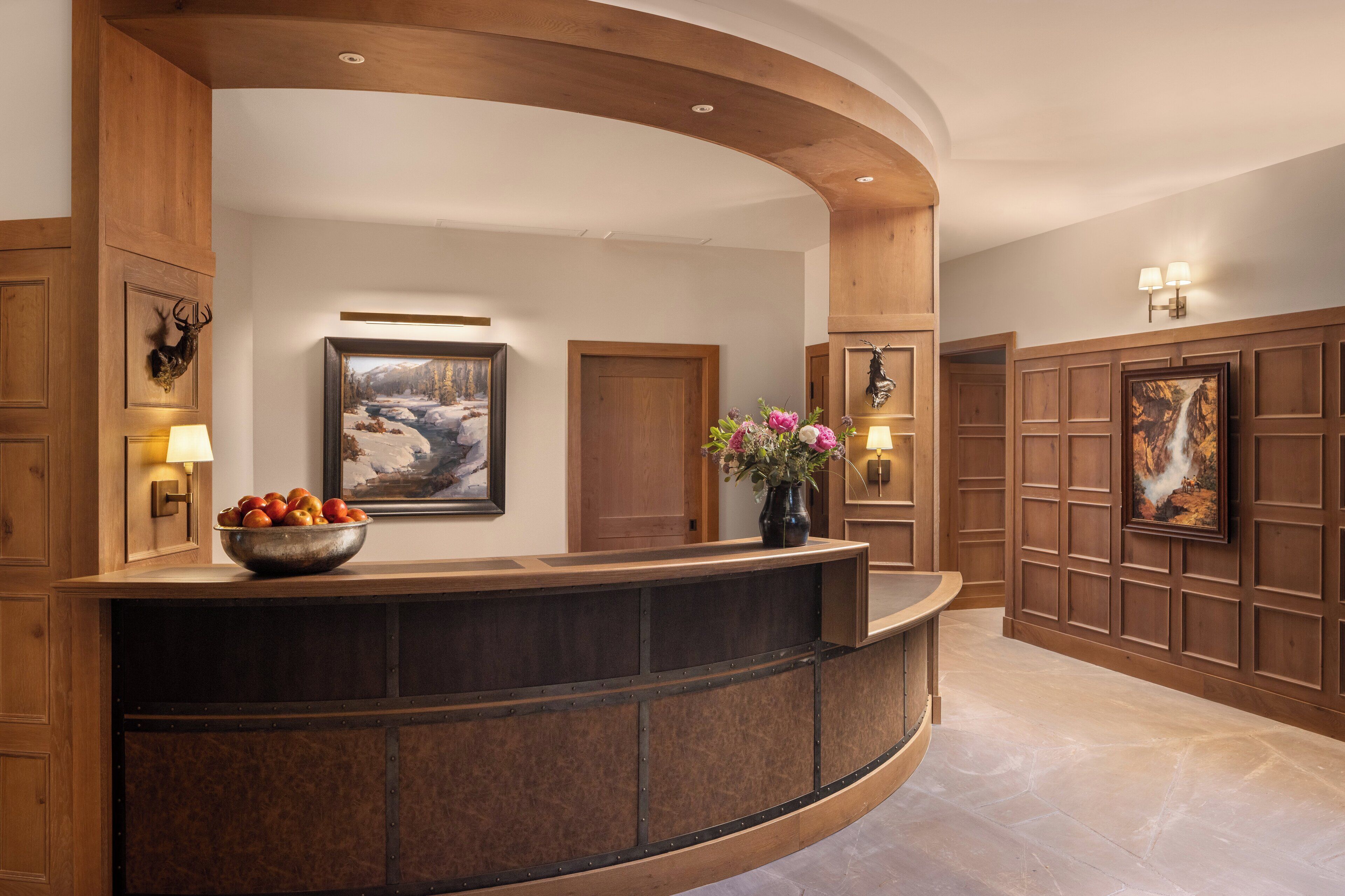 A reception area with a curved wooden reception desk, framed artwork on the walls, and a vase with flowers.