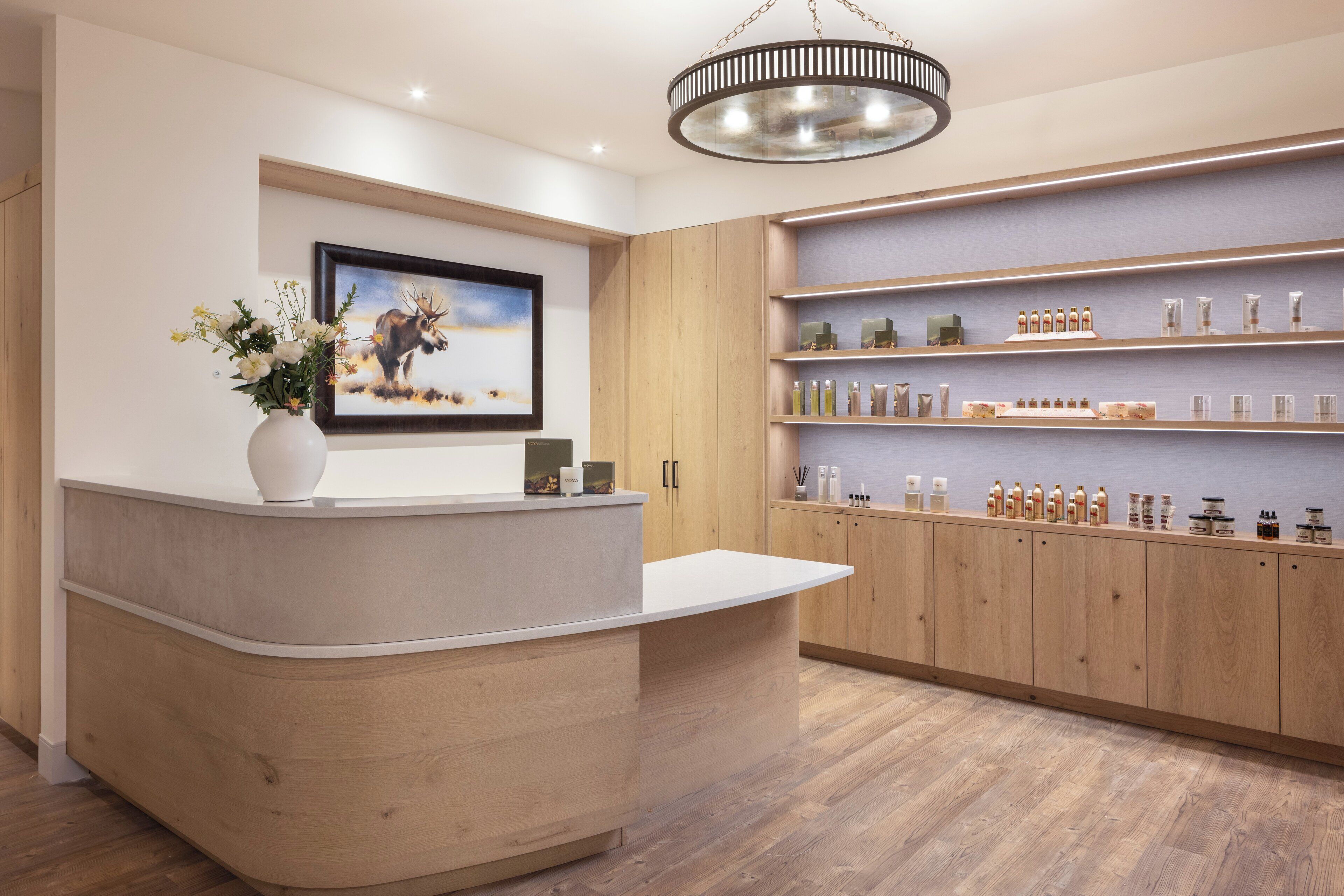 A reception area with a wooden reception desk, a framed wildlife painting, a vase of flowers, and shelves with various products.