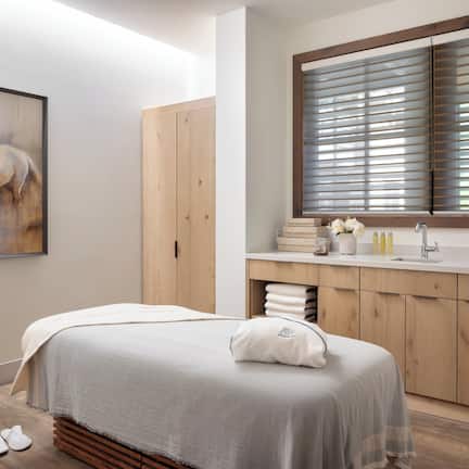 A bedroom with a bed, a chair, a wooden wardrobe, a window with blinds, and a painting on the wall.