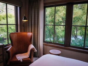 A room with a large window, a chair, a small round table, and a lamp.