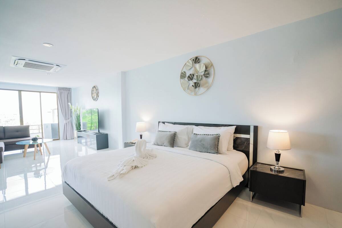 A modern hotel room with a large bed, bedside lamps, a flat-screen TV, and a view of the outdoors.