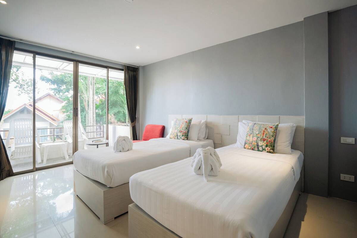 A hotel room with two beds, a balcony, and a view of the outside.