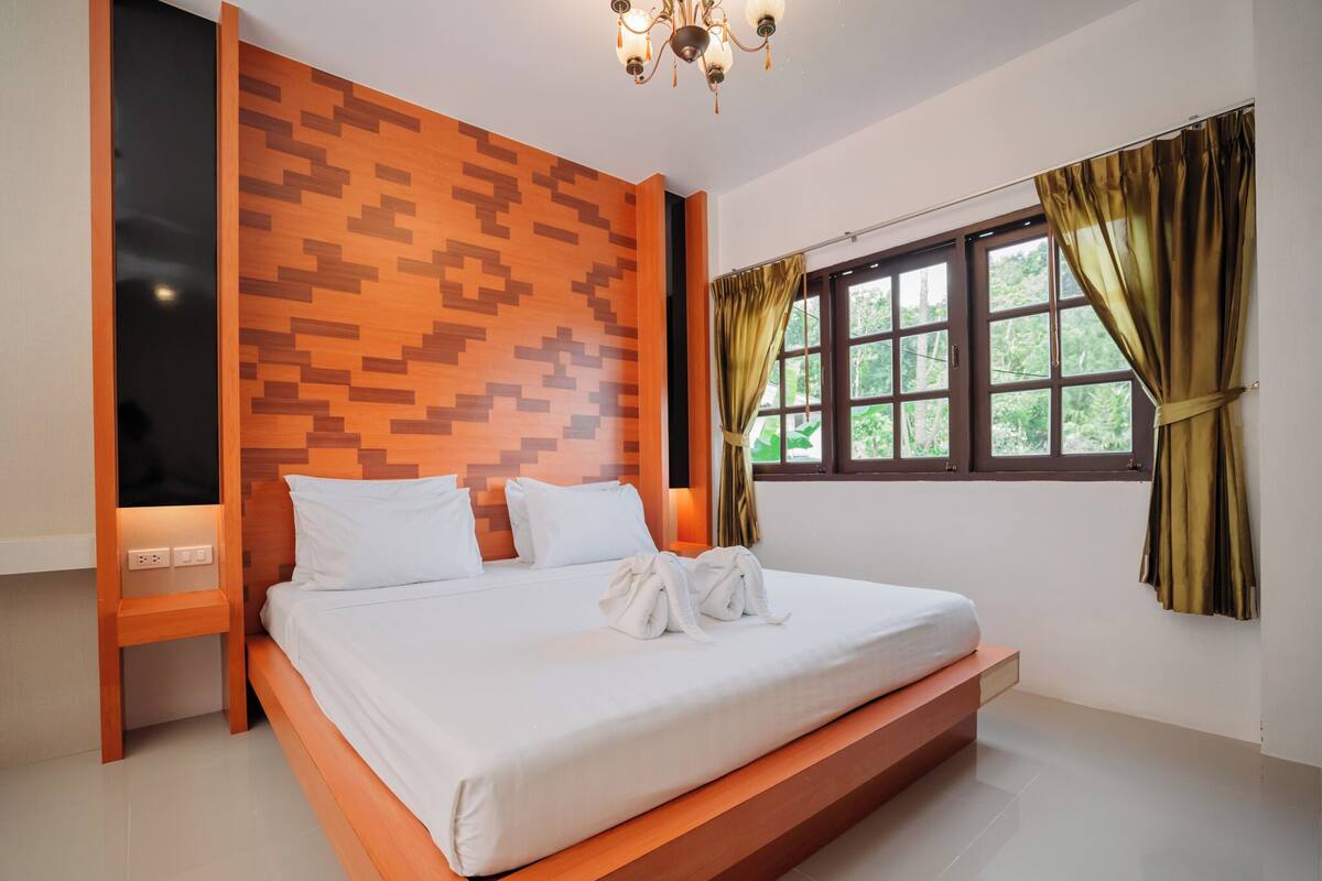 A modern hotel room with a large bed, a wooden headboard, a TV, and a window with curtains.