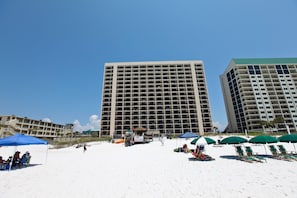 A beach with a large hotel building, beach chairs, umbrellas, and a lifeguard stand. - SunDestin Beach Resort (Destin)