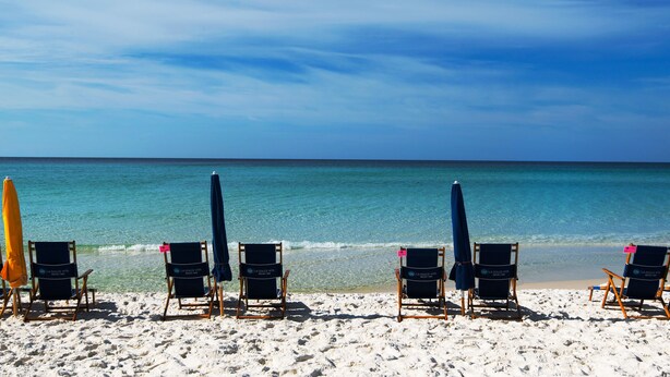 A beach with several lounge chairs and umbrellas, arranged in a row facing the ocean. - SunDestin Beach Resort (Destin)
