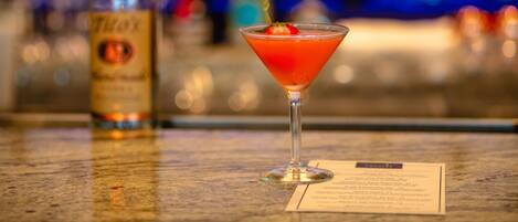 A martini glass with a garnish on a bar counter, a bottle of liquor, and a menu.