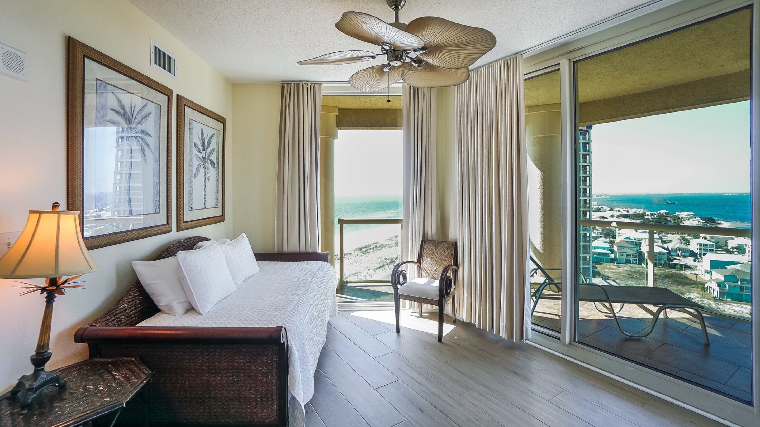 Ein Hotelzimmer mit Bett, Stuhl, Lampe und einem Balkon mit Blick auf Strand und Meer.