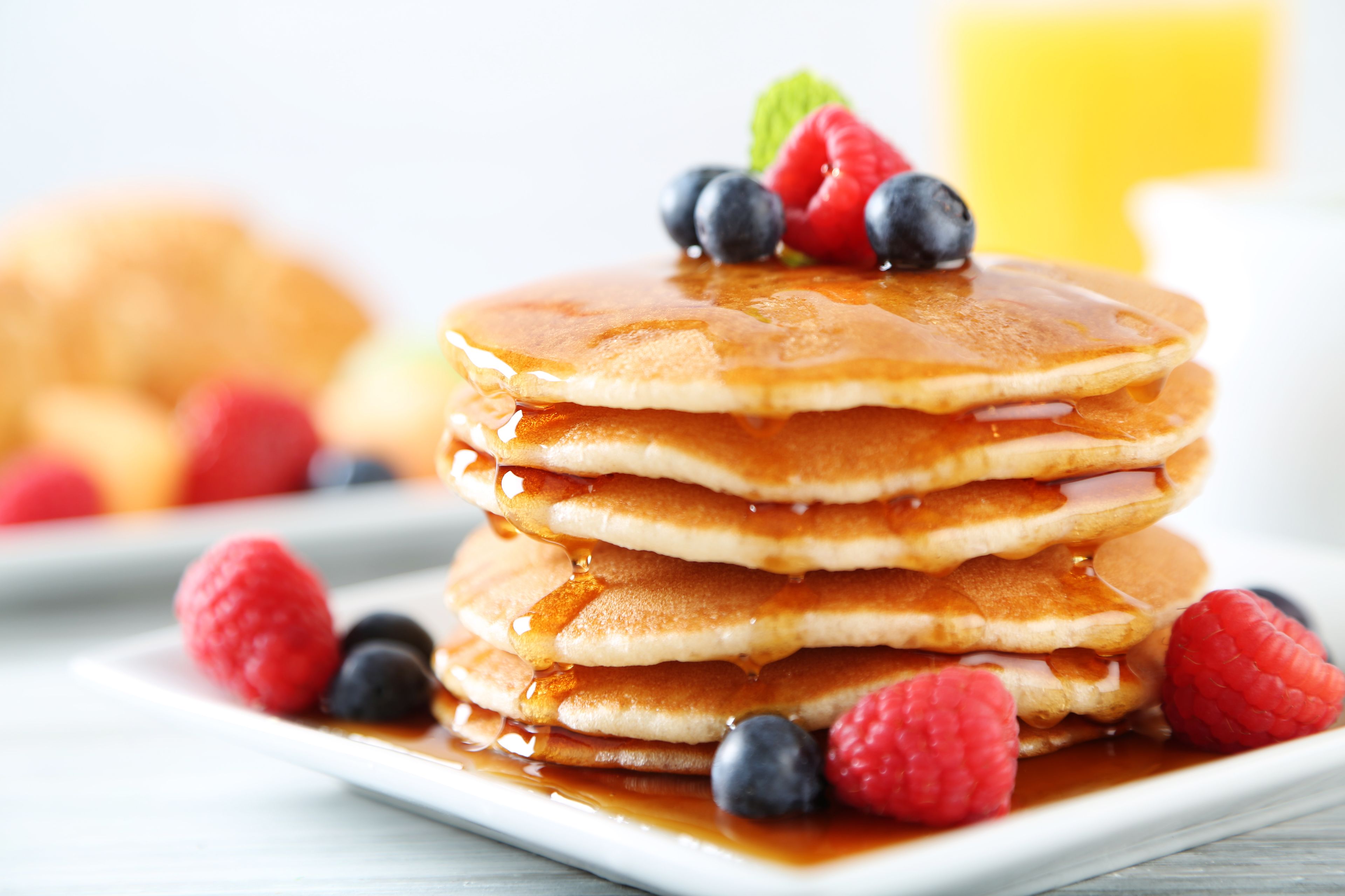 Une pile de crêpes arrosées de sirop et garnies de fruits rouges.